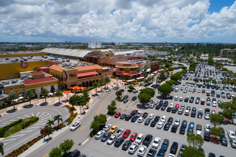 Aerial view of Dolphin Mall in Sweetwater, Florida, showing the large shopping complex, restaurants, surrounding parking lots, and palm-lined streets on a sunny day.