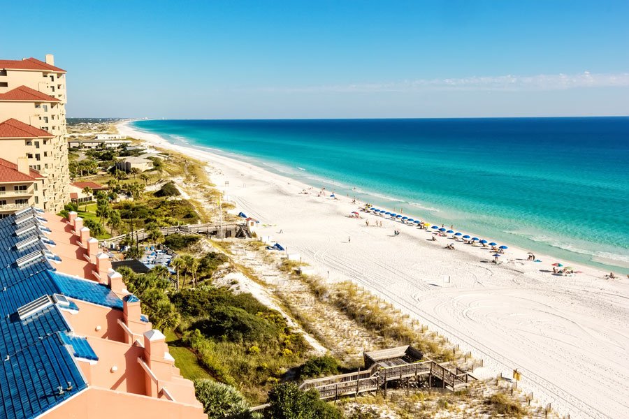 Elevated view of Miramar Beach’s emerald-green Gulf waters and wide sandy shoreline, with beachfront resorts and rental properties overlooking the coast.