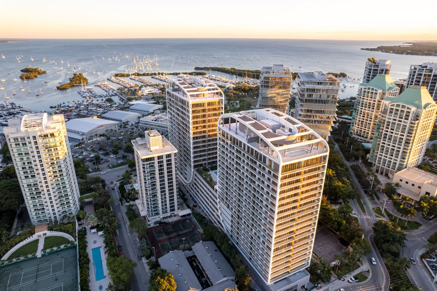 Aerial view of Coconut Grove, Florida, showing waterfront high-rise residences, marinas filled with sailboats, and Biscayne Bay stretching into the distance at sunset.