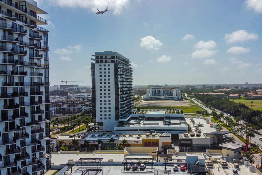 Aerial view of Downtown Doral, Florida, showing modern residential towers, mixed-use development, and nearby roadways, with an aircraft visible overhead reflecting the city’s proximity to Miami International Airport.