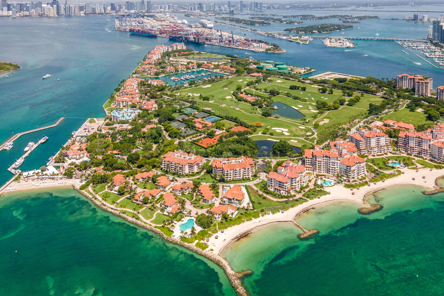 Aerial view of Fisher Island, Florida, showing its private residences, golf course, marina areas, and waterfront setting at the entrance to Biscayne Bay near Miami.