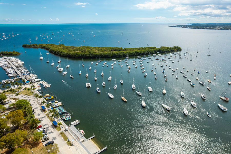 Aerial view of Dinner Key Picnic Islands Park in Coconut Grove, Miami, showing sailboats anchored across Biscayne Bay and marina facilities along the waterfront. Photographed February 27, 2025.