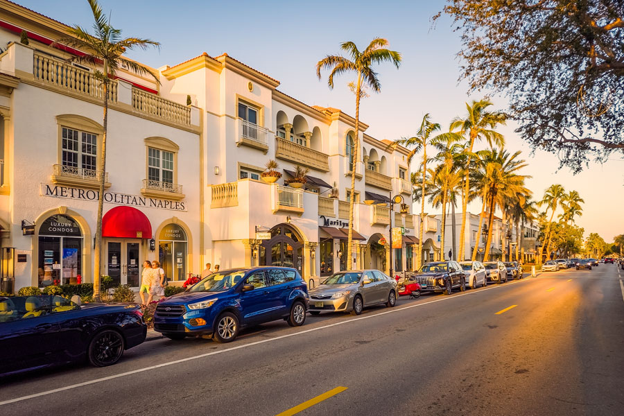 Street view of downtown Naples, Florida, featuring Mediterranean-style architecture, palm-lined sidewalks, and a mix of shops, dining, and residential buildings along one of the city’s walkable commercial districts.