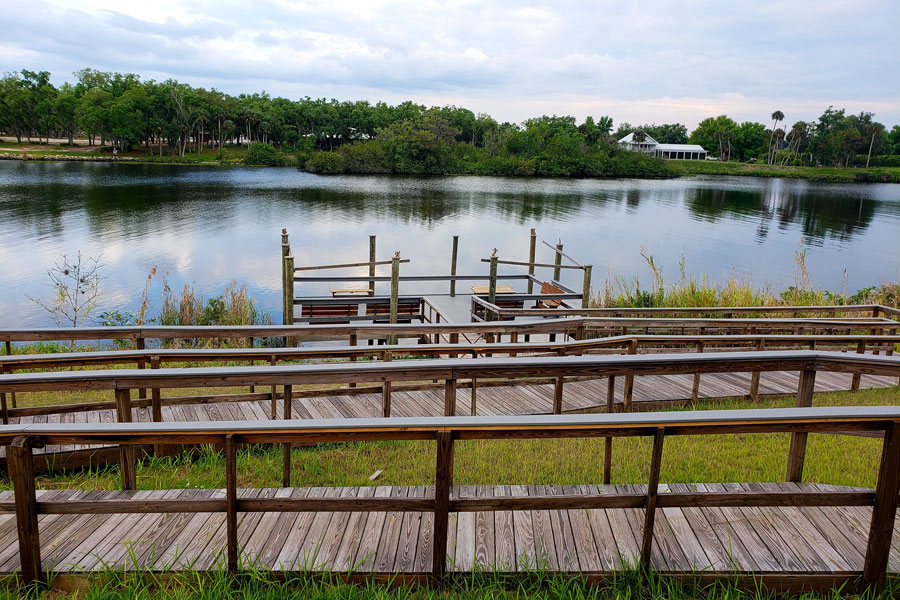 A wooden boardwalk and fishing pier lead to the Caloosahatchee River in Fort Denaud, a rural community near LaBelle in Hendry County. The 67-mile river flows west across Southwest Florida toward the Gulf of Mexico, connecting inland communities with the coast.