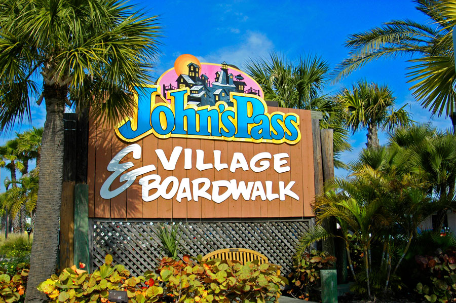 Randy Pr The colorful John’s Pass Village & Boardwalk entrance sign welcomes visitors to the popular waterfront district in Madeira Beach, surrounded by palms and tropical landscaping. The village is known for its boardwalk, shops, restaurants, fishing charters, sightseeing cruises, and views of John’s Pass.