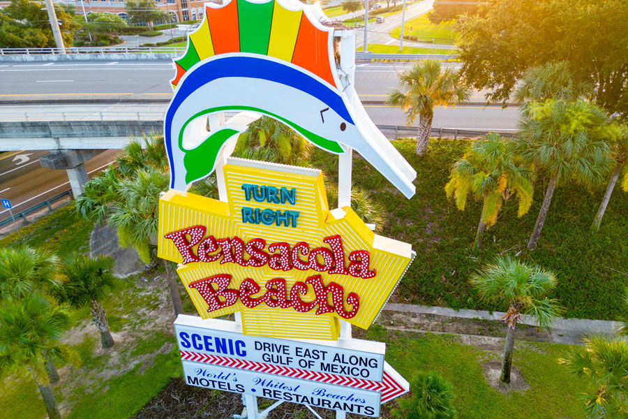 The colorful Pensacola Beach welcome sign stands near the gateway to Santa Rosa Island, greeting visitors arriving at one of Florida’s best-known Gulf Coast beach communities. The landmark points the way toward the shoreline, local restaurants, motels, and the Gulf of Mexico. 