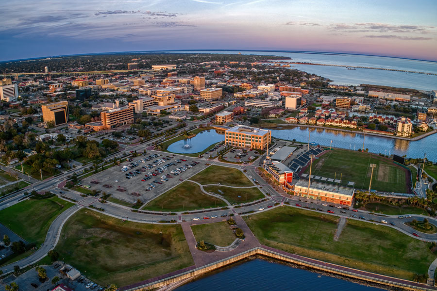 An aerial view of downtown Pensacola at sunset, with the city’s waterfront, parks, marina, and Blue Wahoos Stadium along Pensacola Bay. The scene highlights Pensacola’s compact downtown core and its close connection to the bayfront.