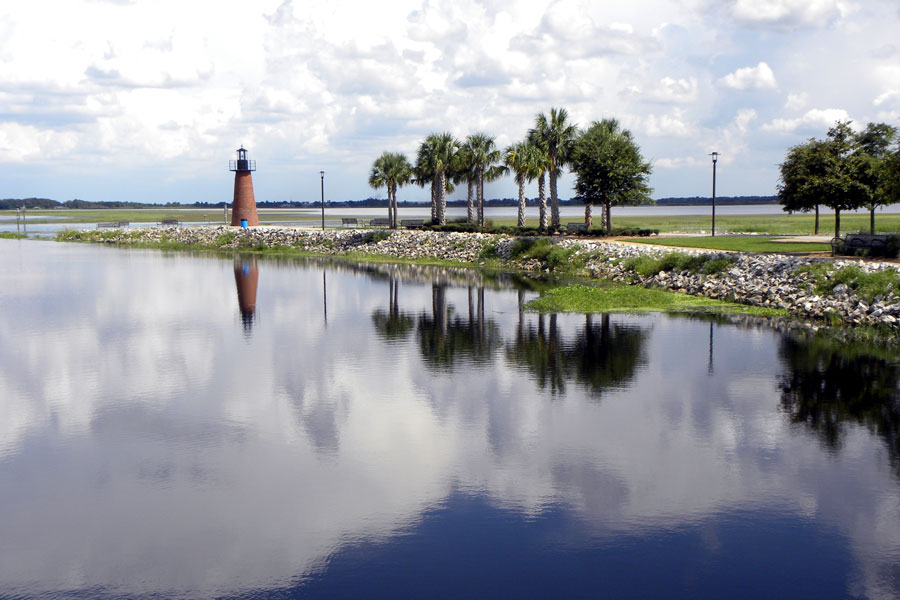A scenic view of Lake Tohopekaliga from Kissimmee Lakefront Park in Kissimmee, Florida, featuring the park's distinctive lighthouse and surrounding trees along the waterfront. Commonly known as Lake Toho, this expansive freshwater lake is a popular Central Florida destination for boating, bass fishing, birdwatching and outdoor recreation, while the lakefront park offers walking paths, picnic areas and scenic views. Photo credit: Chris Mercer, licensed.