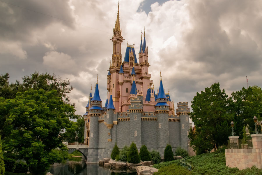 Cinderella Castle rises above the landscaped grounds of Magic Kingdom at Walt Disney World Resort in Bay Lake, Florida, with its pink towers, blue rooftops and ornate spires standing beneath a dramatic cloudy sky. One of Central Florida's most recognizable landmarks, the castle serves as the centerpiece of Magic Kingdom, a major attraction drawing millions of visitors to the Orlando area each year. Photo credit: dorengo5, licensed.