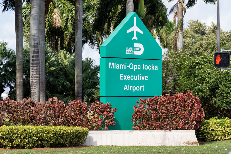 The entrance sign for Miami-Opa Locka Executive Airport (OPF) stands among palm trees and landscaped grounds in Opa-locka, Miami-Dade County, Florida. The airport serves private and corporate aviation, flight training, and specialized aircraft operations throughout the Greater Miami area. Originally established in 1927, the facility also has a long history of military aviation and remains home to U.S. Coast Guard Air Station Miami. Photo credit: JHVEPhoto; licensed.