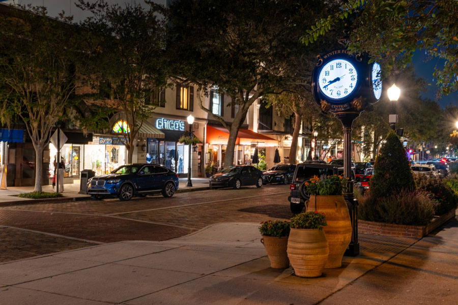 Park Avenue in downtown Winter Park, Florida, comes alive after dark, with illuminated storefronts, restaurants, brick-paved streets and the historic street clock creating a welcoming evening atmosphere. Located just north of Orlando, Winter Park is known for its walkable downtown, upscale shopping, dining, cultural attractions and picturesque tree-lined streets. Photo credit: efiederphoto, licensed.