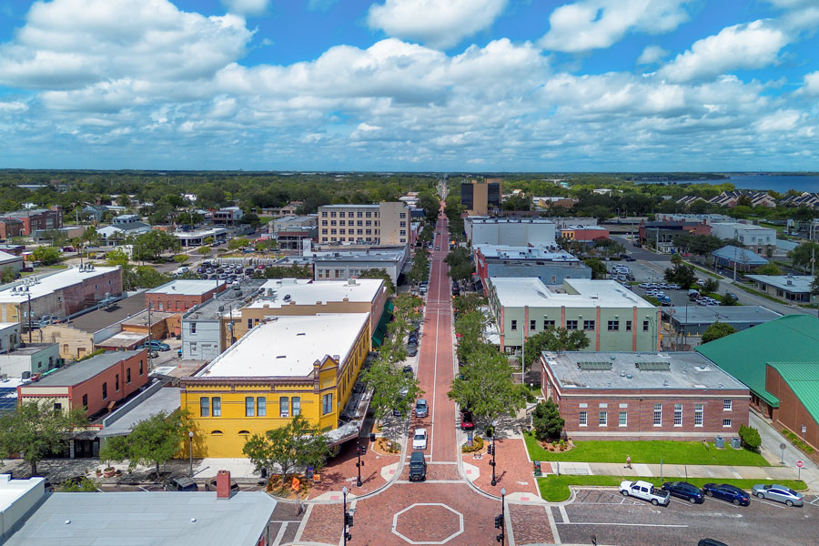 An aerial view of historic downtown Sanford, Florida, looking along the brick-paved First Street corridor, with colorful historic buildings, tree-lined sidewalks and local businesses extending toward the waterfront. Located along Lake Monroe in Central Florida, Sanford is known for its preserved downtown architecture, restaurants, shops, cultural attractions and connection to the St. Johns River. Photo credit: Lucky-photographer, licensed.