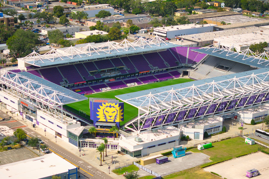 An aerial view of Inter&Co Stadium in downtown Orlando, Florida, showcasing the soccer field, purple seating and distinctive open-air architecture of the home stadium for Orlando City SC and Orlando Pride. Located in the Parramore neighborhood west of downtown Orlando, the stadium is a major Central Florida sports venue, hosting professional soccer matches and other events that contribute to the region's growing sports and entertainment scene. Photo credit: 4kclips, licensed.